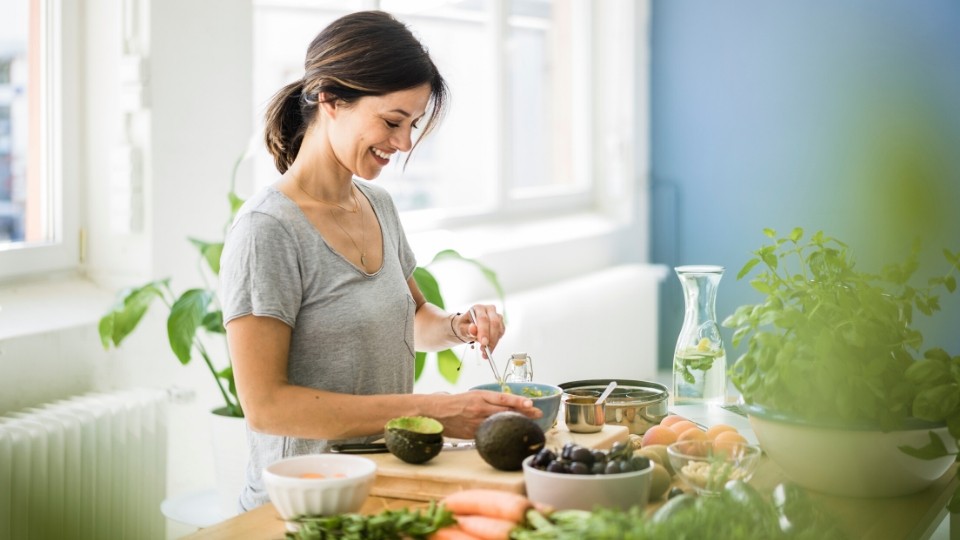 A young woman cuts up avocado in the kitchen while smiling