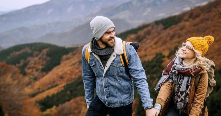 A man and a woman walking on a hillside holding hands and smiling at each other