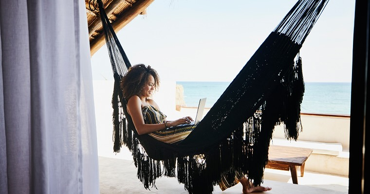 A woman sitting on a hammock while working on a laptop