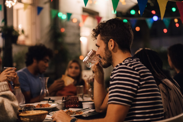 Man in striped shirt drinking at dinner table with friends.