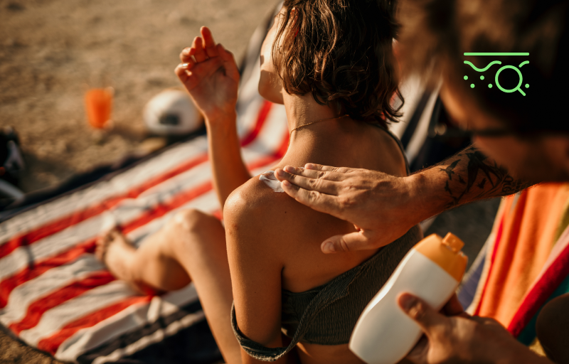 Man helping woman put on sunscreen at beach.