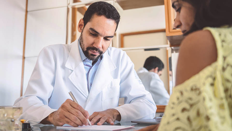 A male doctor fills out a form as his female patient sits across from him