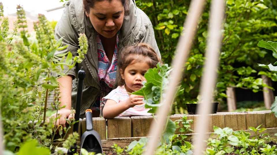 A woman picking produce from a veggie patch with her daughter.