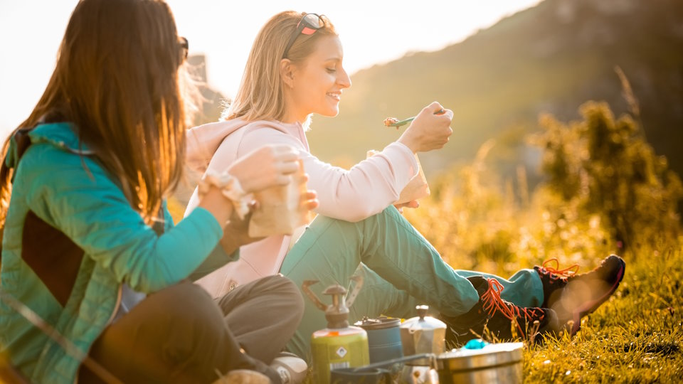 Two people sitting at a campsite on a mountain, eating camping food.