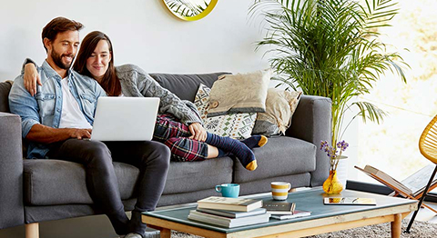 A man and a woman sitting on a couch looking at a laptop