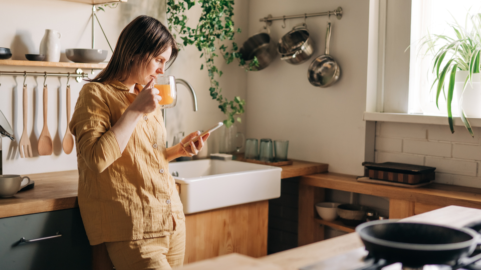 35 yr old woman wearing yellow linen top in her kitchen looking at her phone