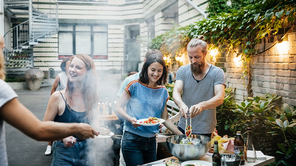 A group of friends laughing and serving themselves food at a backyard gathering