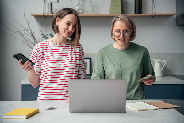 Two joyful women with a laptops at kitchen