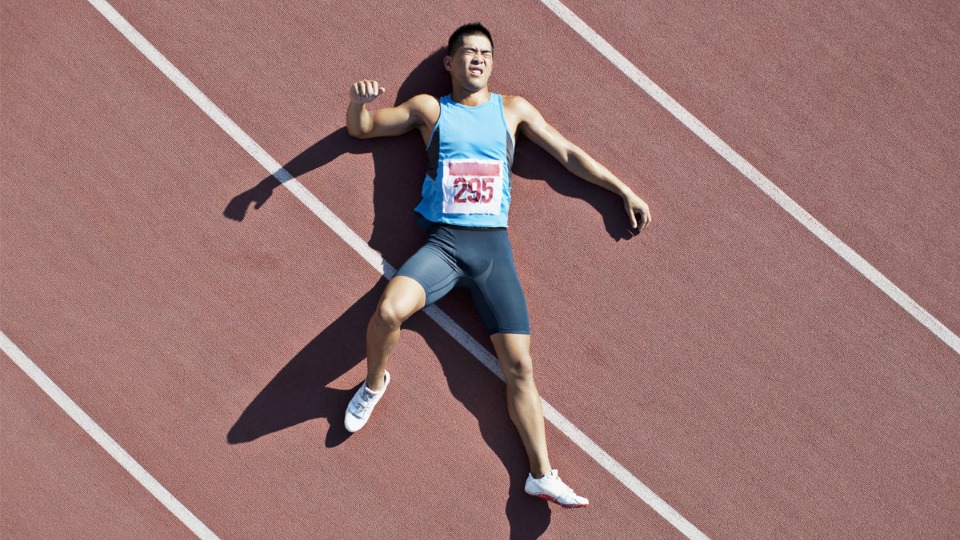 A young athlete grimaces as he lays on a running track