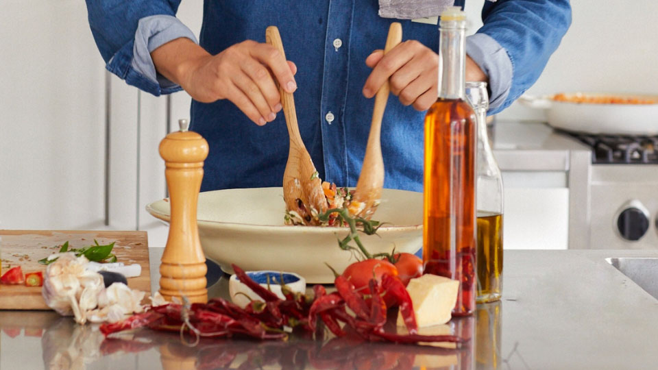 Close up of a person tossing a salad with dried chilis in the foreground.