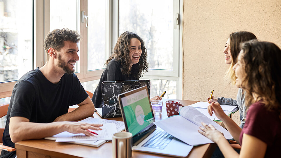 A group of young people laugh as they share study notes at a table