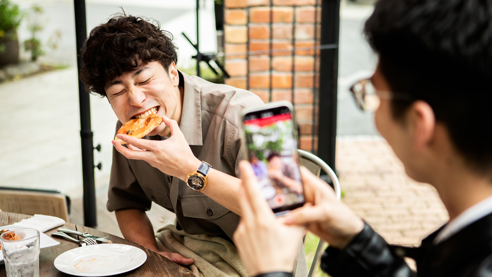 One person taking a photo of another person eating at a cafe.