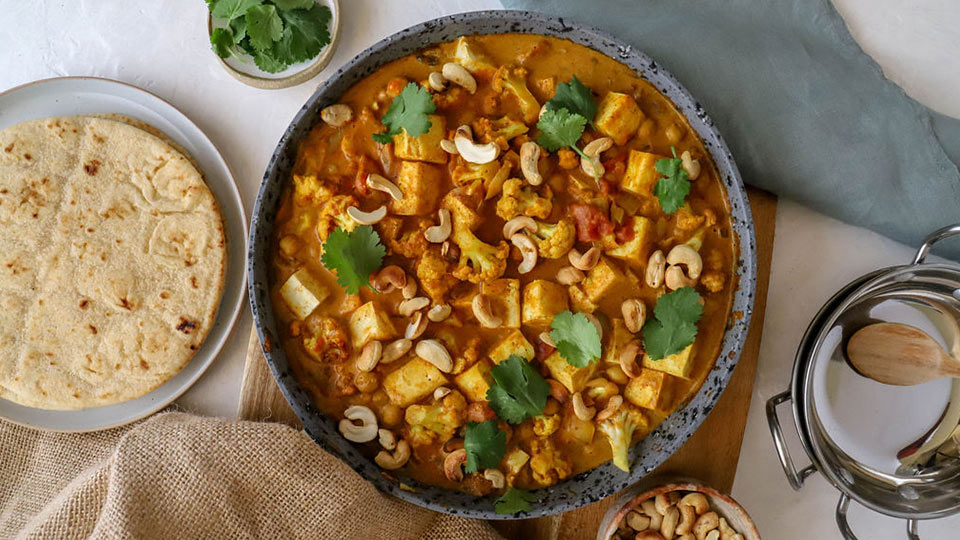 Chicken curry in a serving bowl on a table with flat bread on the side.