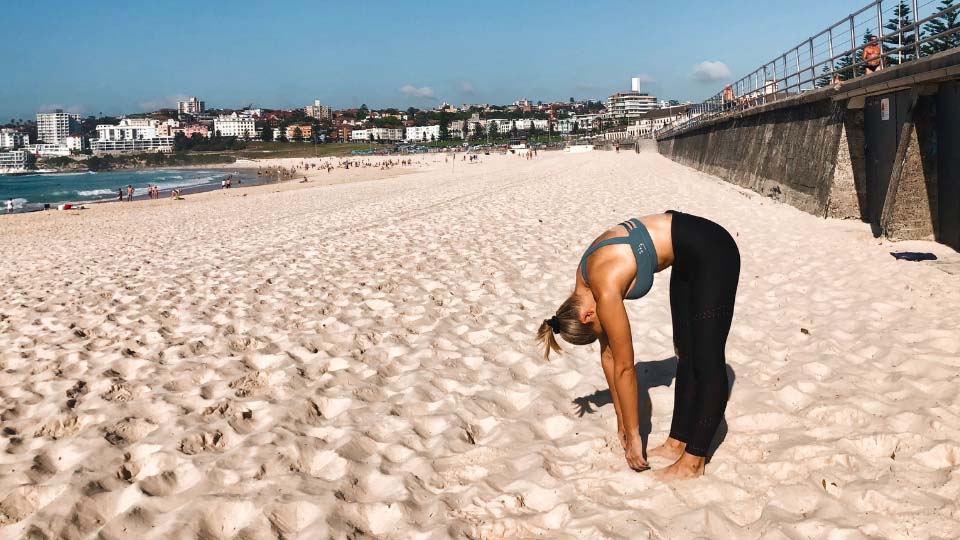 Cassey Maynard standing up and bending over to touch her toes at the beach.