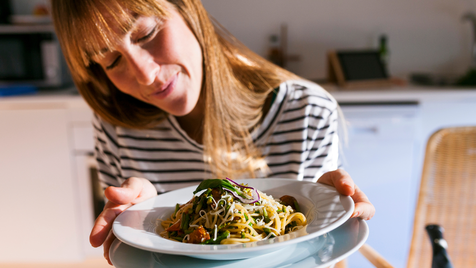 30 year old woman with a blue and white striped shirt looking at a bowl of fresh pasta.