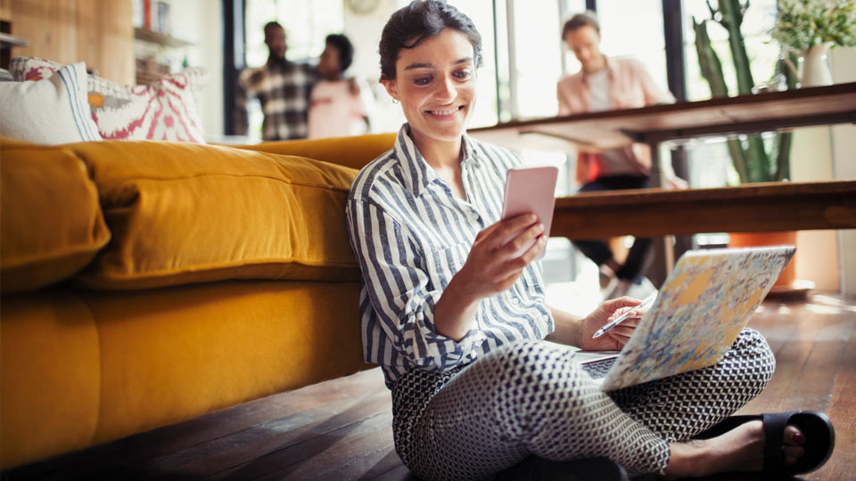 Woman sitting on floor with her phone and laptop.