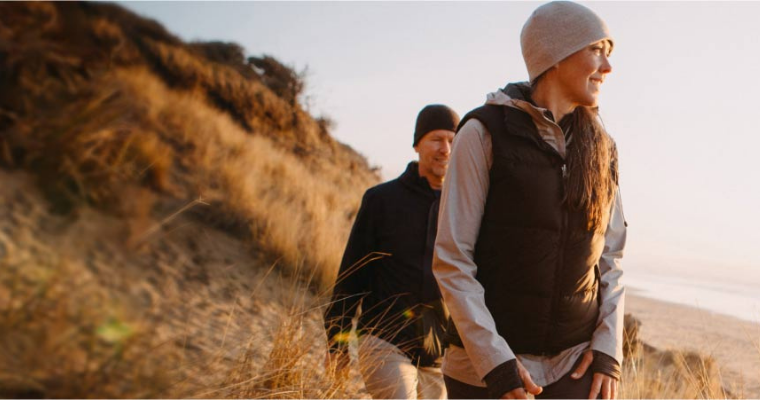 A man and a woman wearing warm clothes walking along a beach