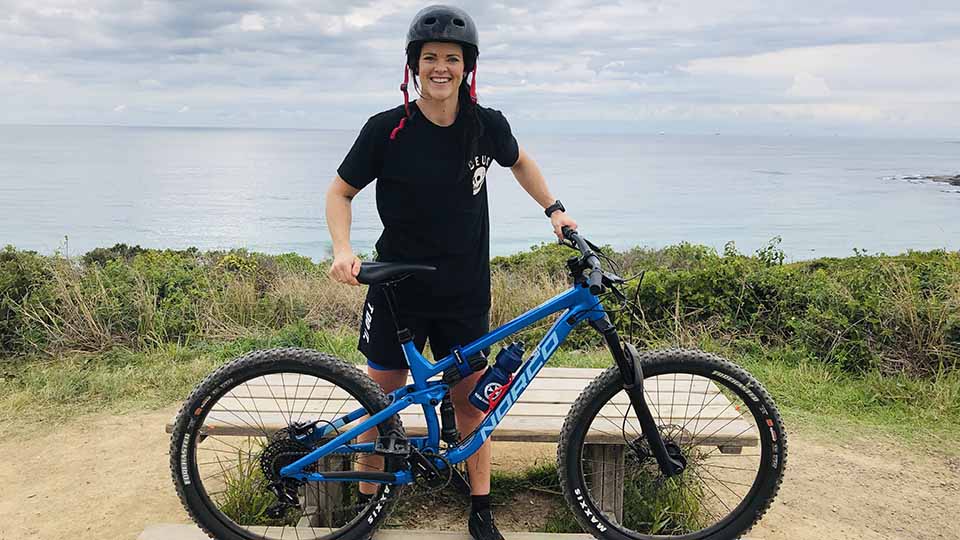 Woman holding a bicycle with the ocean in the background.