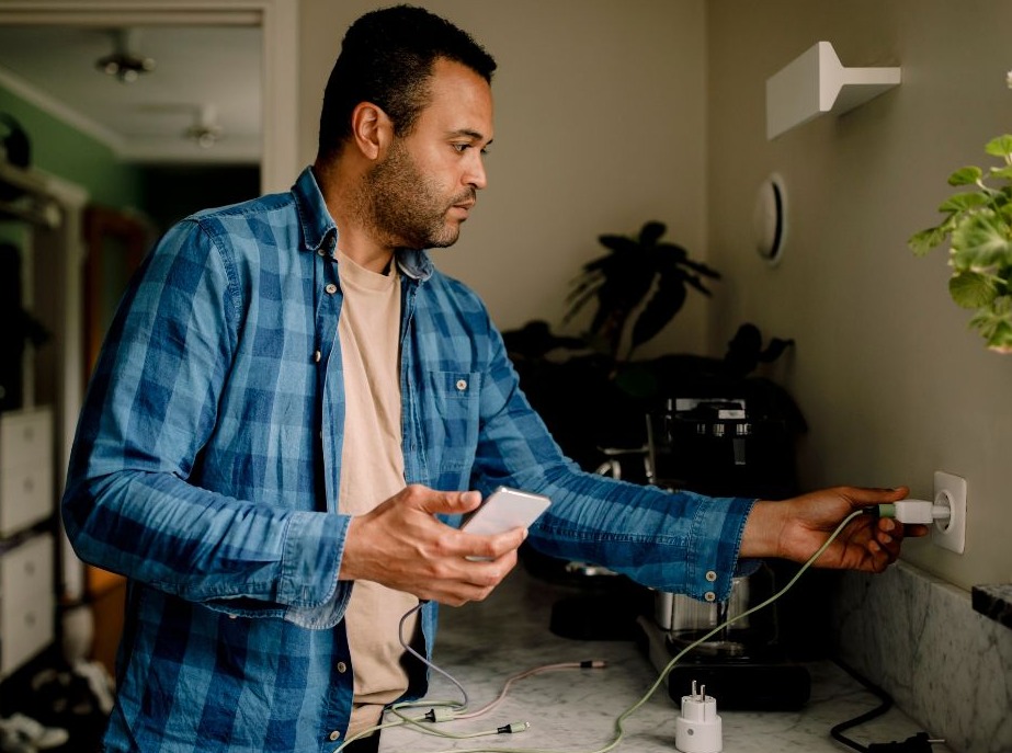 Person standing in a kitchen unplugging their digital devices from chargers.