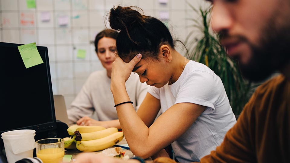 Woman leaning on desk holding her head, trying to determine if she has a headache or migraine.