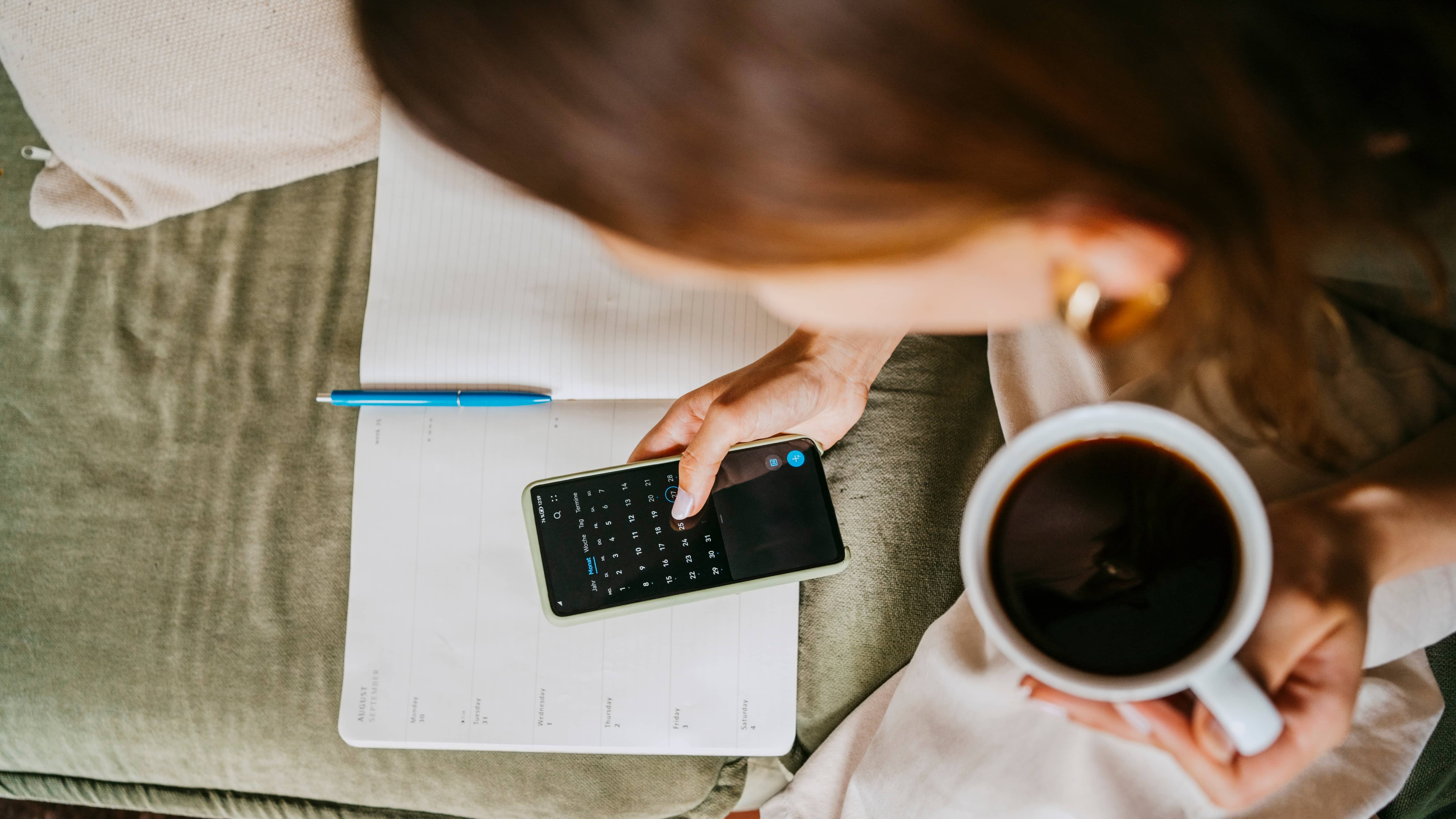 Person looking at a calendar on their phone while drinking coffee.