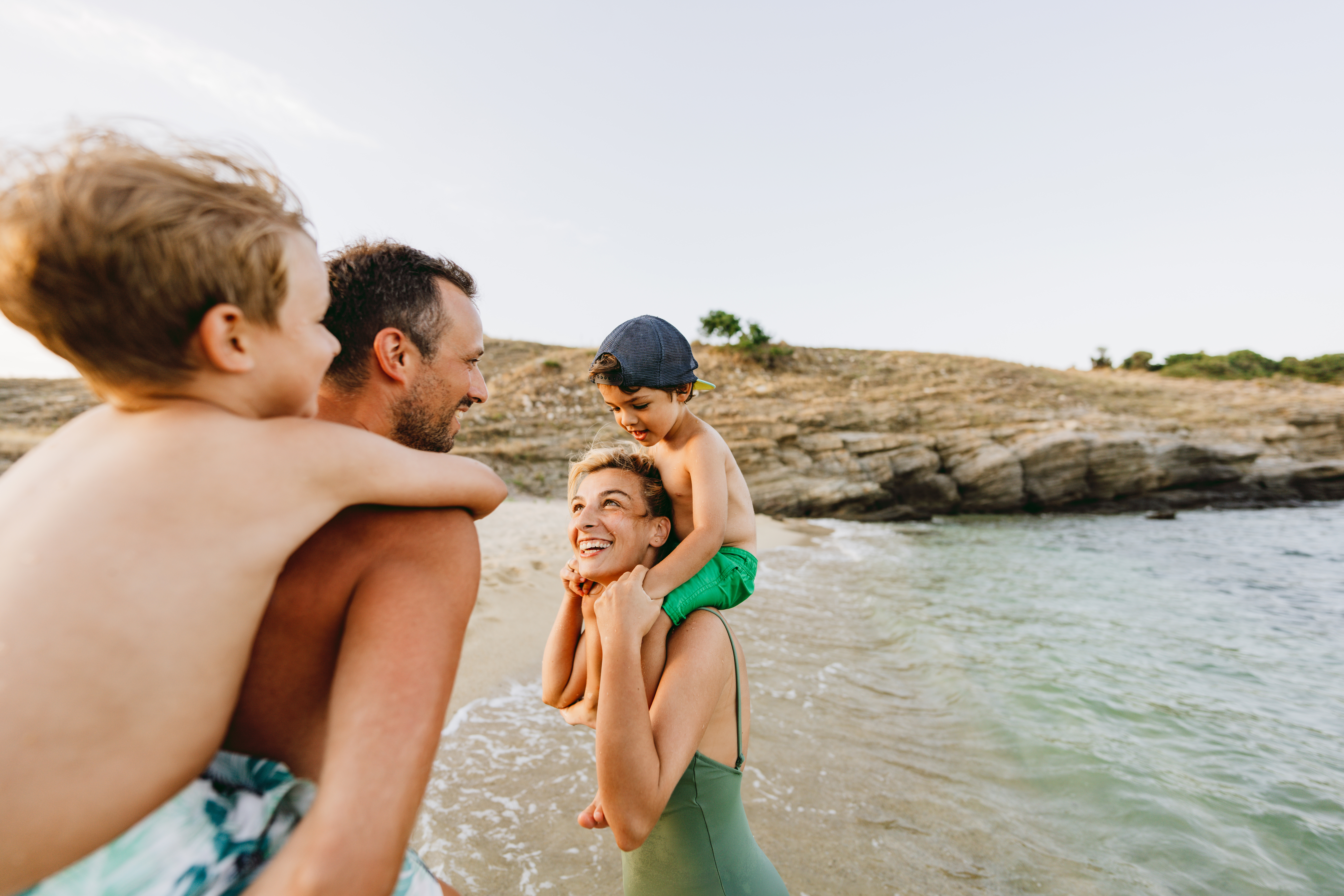 Smiling couple playing with two young children on a sandy beach near the water.