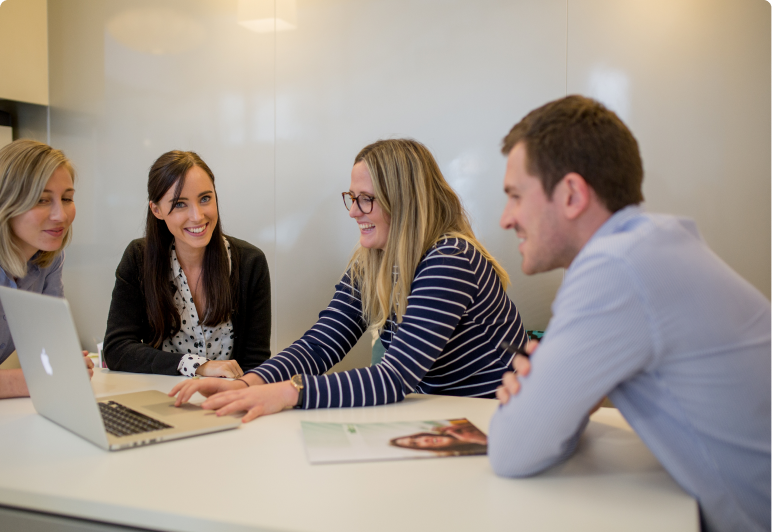Four people sit around a table looking at a laptop