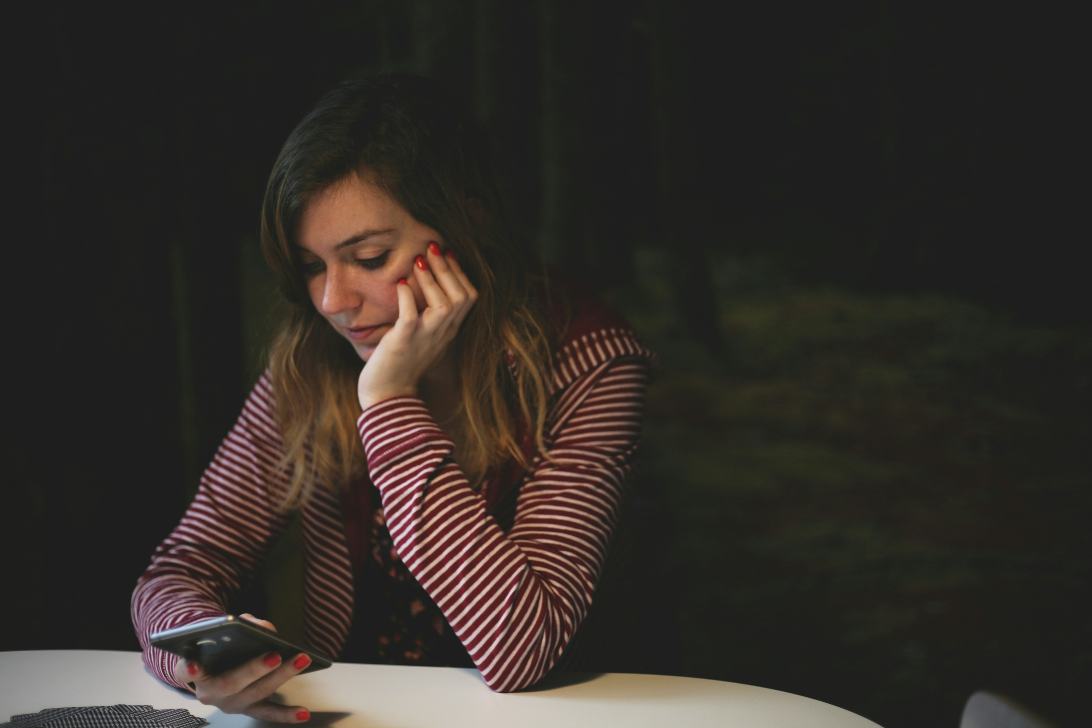 woman leaning on white wooden table while holding black smartphone