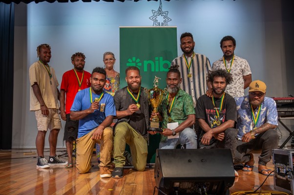 A group of PALM scheme workers wearing medals around their necks and standing in front of a nib poster