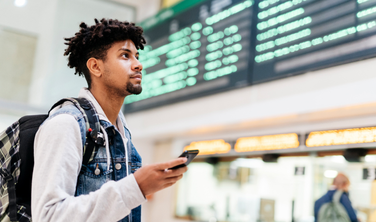 A man on his phone looking at the departures board at an airport