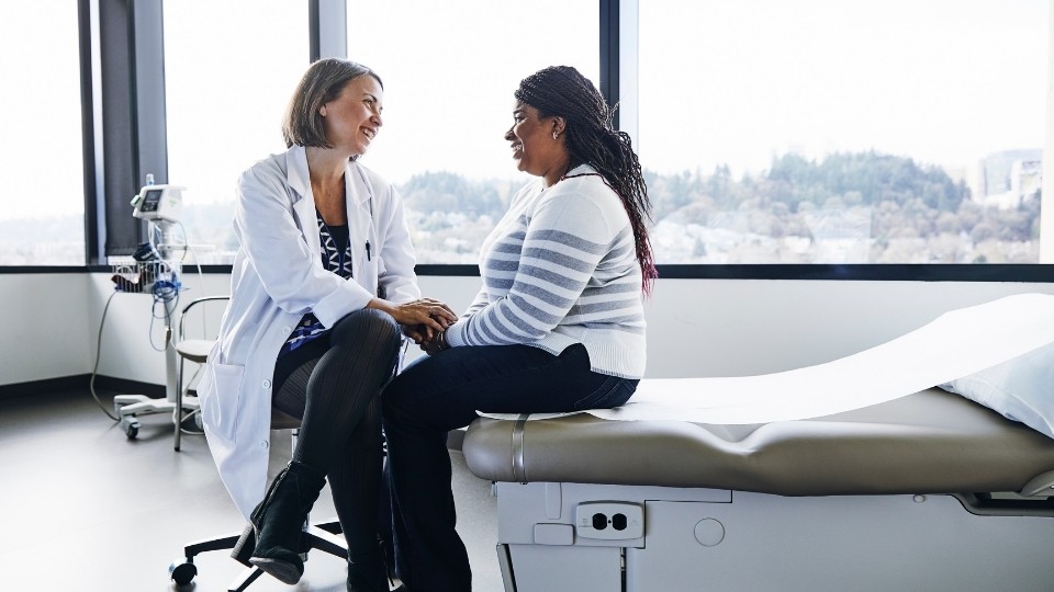 Woman sitting on the edge of a hospital bed talking to a doctor.