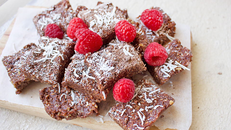 Stack of chocolate brownies with raspberries and coconut on top.