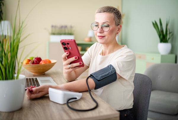 A woman checks her blood pressure at home while checking her phone
