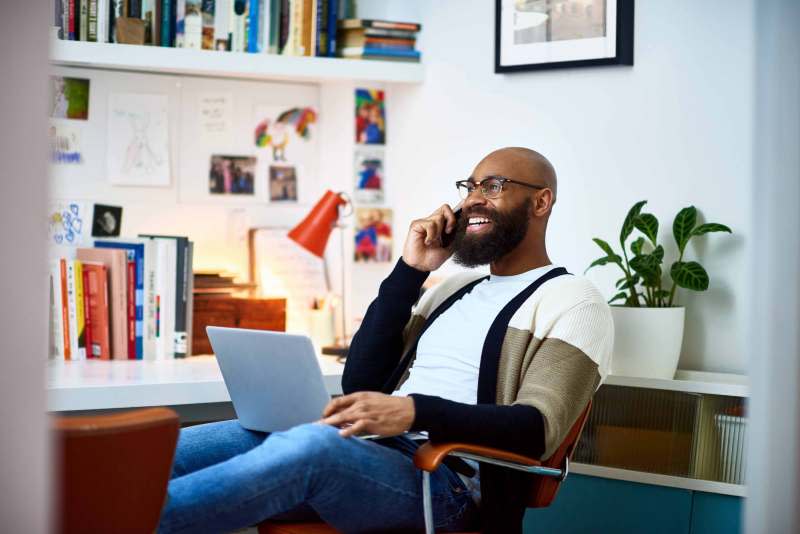A cheerful looking person talking on the phone while they hold a laptop.