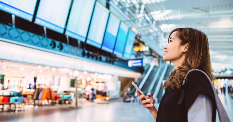 A woman at an airport holding a phone while looking at the departures board
