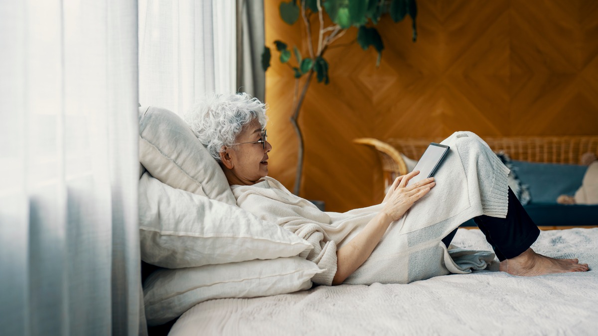 A woman lays on her bed looking at her tablet device.