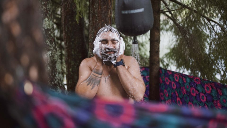 Man showering in outdoor camping shower with a foamy lather of soap on his face.