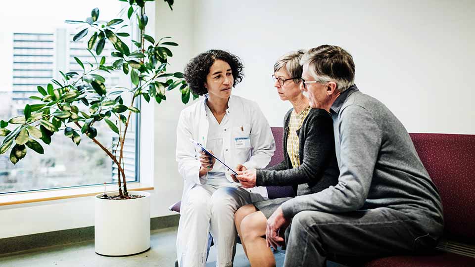 Two people sitting with a doctor having information read to them from a chart.