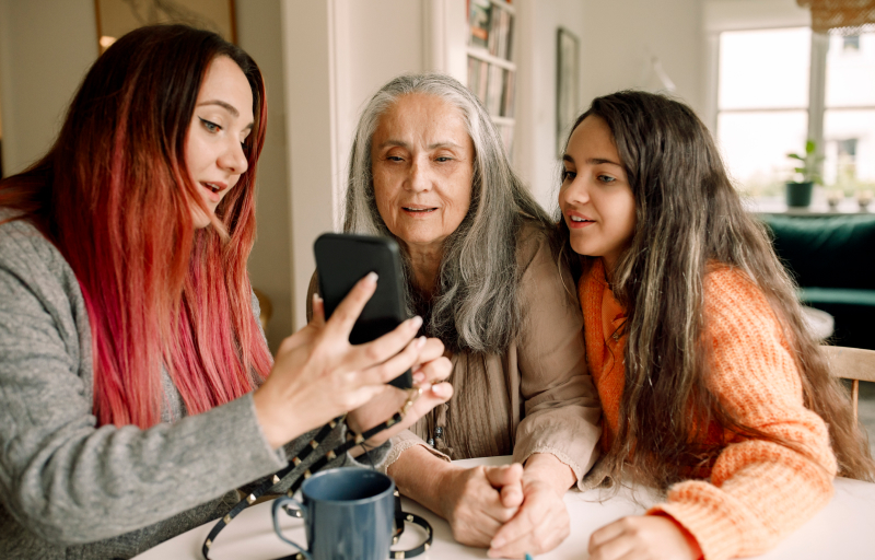 Woman with pink dyed hair showing phone to mother and her sister
