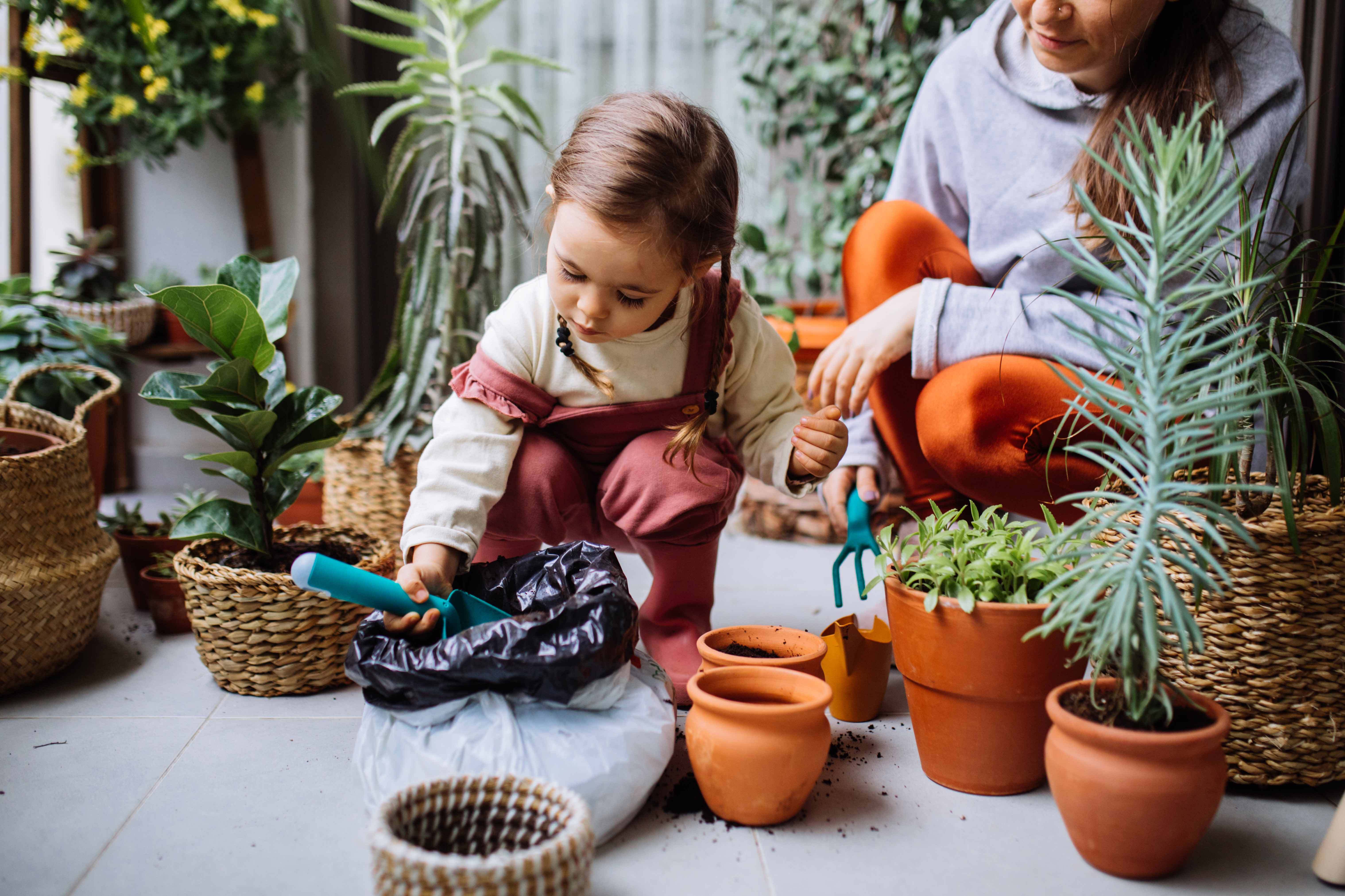 Cute Girl Planting Flowers With Mother At House Balcony