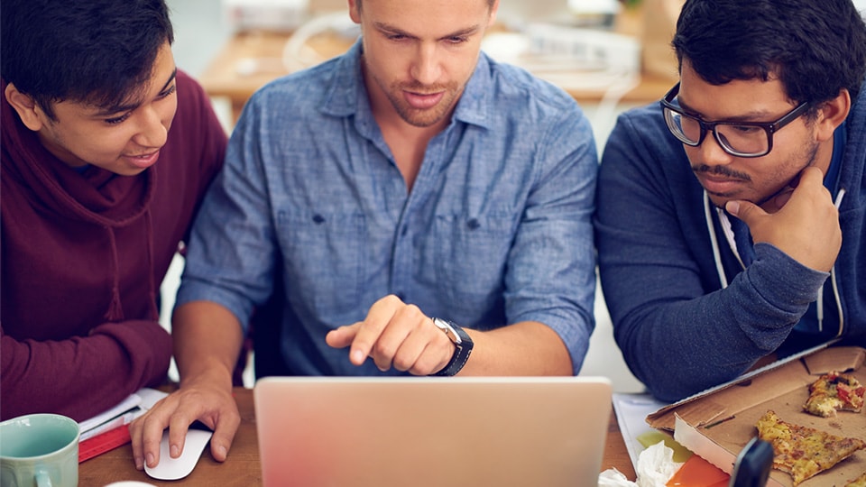 Three people crowding around a laptop computer.