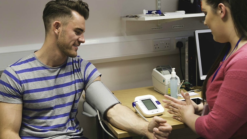 A young man has his blood pressure taken by a female doctor.