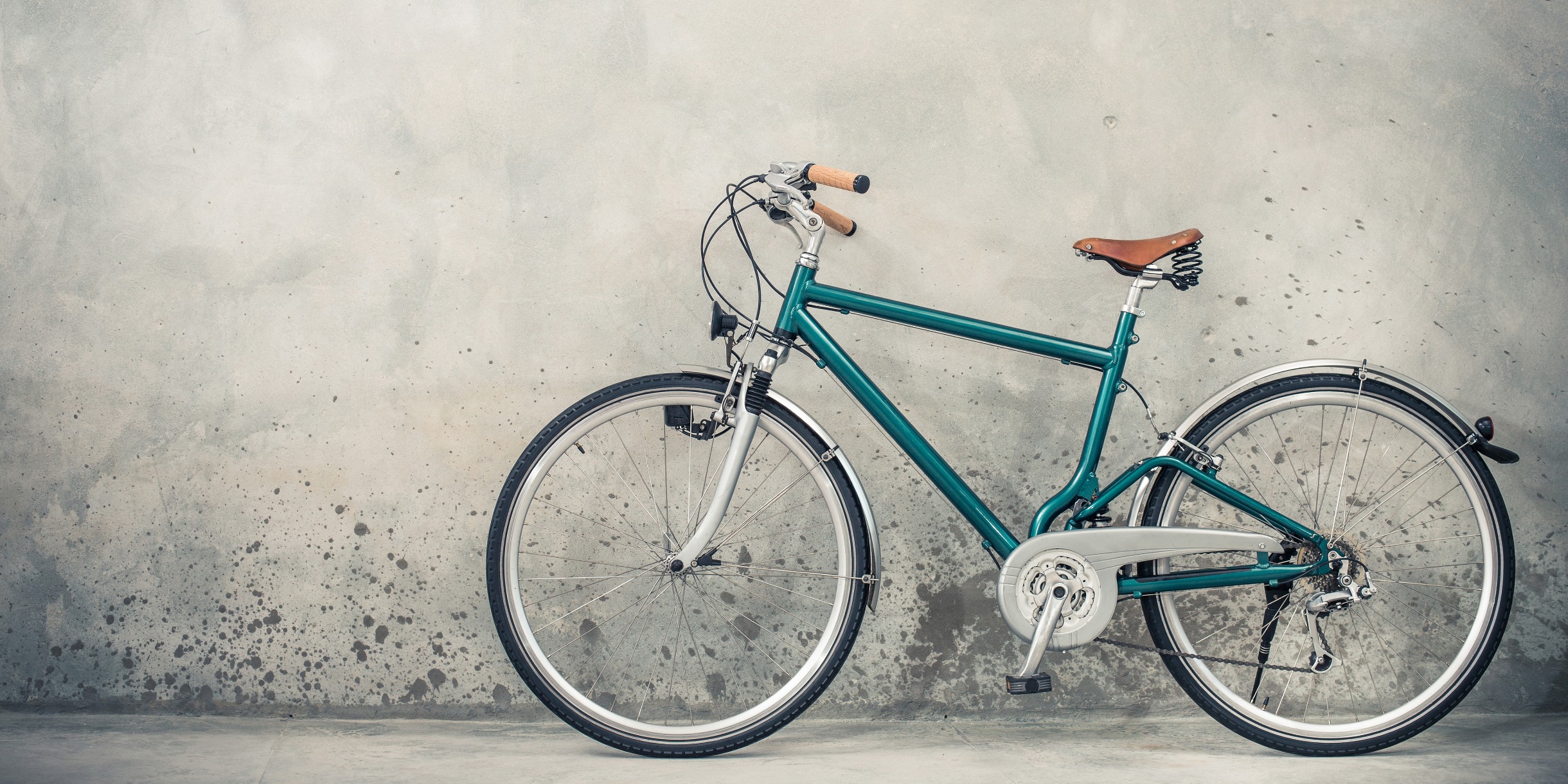 dunkelgrünes Retro Fahrrad mit altem braunen Sattel, etwa aus den 90ern, vor grauer Hauswand.