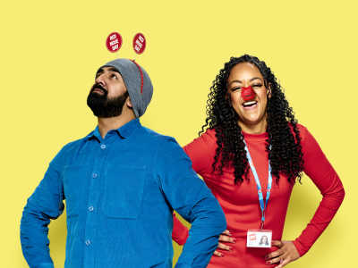 One adult looking up and wearing Red Nose Day antennae and one adult laughing and wearing a red nose