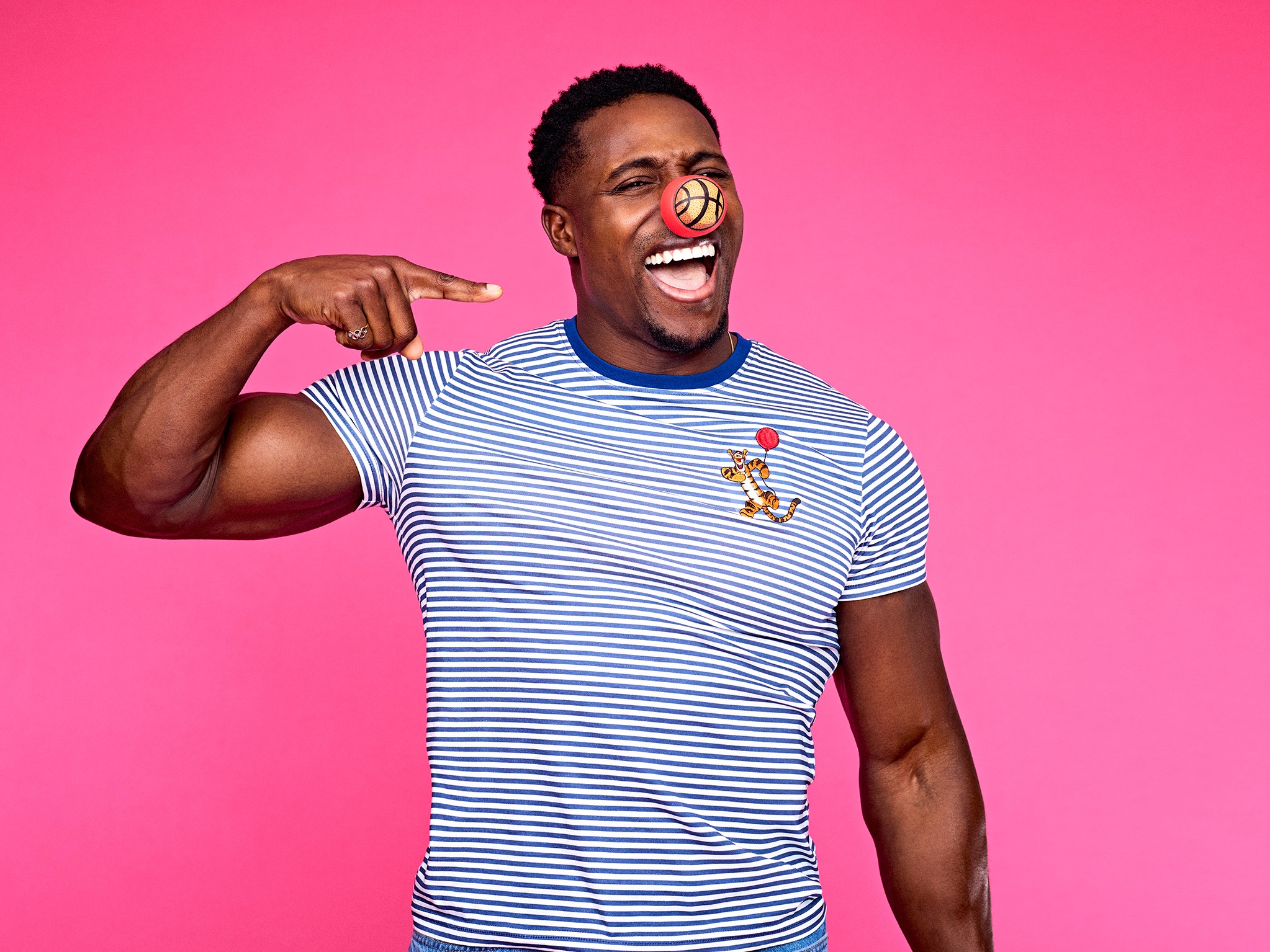 Nitro wears a striped shirt pointing to their chest, set against a bright pink background