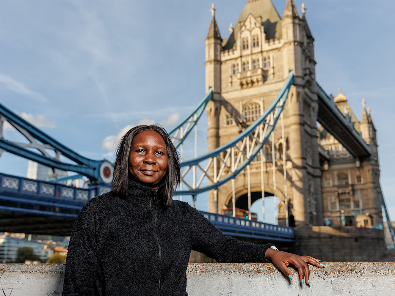 A woman stands in front of a London Bridge.