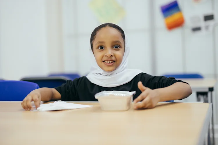 A little girl sat at a desk smiling at the camera
