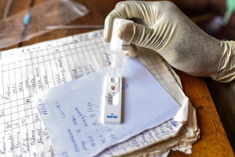 A gloved hand dropping liquid into a lateral flow test