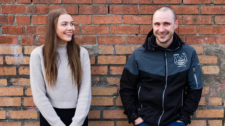 Courtney and Ritchie smiling outside against a brick wall.