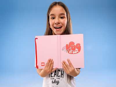 A little girl holding a pink Comic Relief notebook 